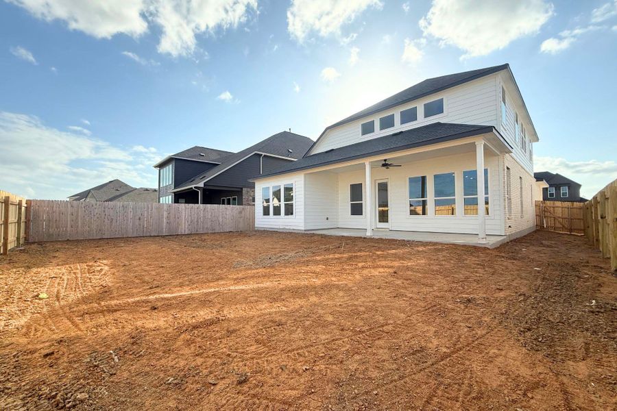 A newly constructed residence features a fenced yard, a rear patio with a ceiling fan, and large windows. A newly constructed residence features a fenced yard, a rear patio with a ceiling fan, and large windows.