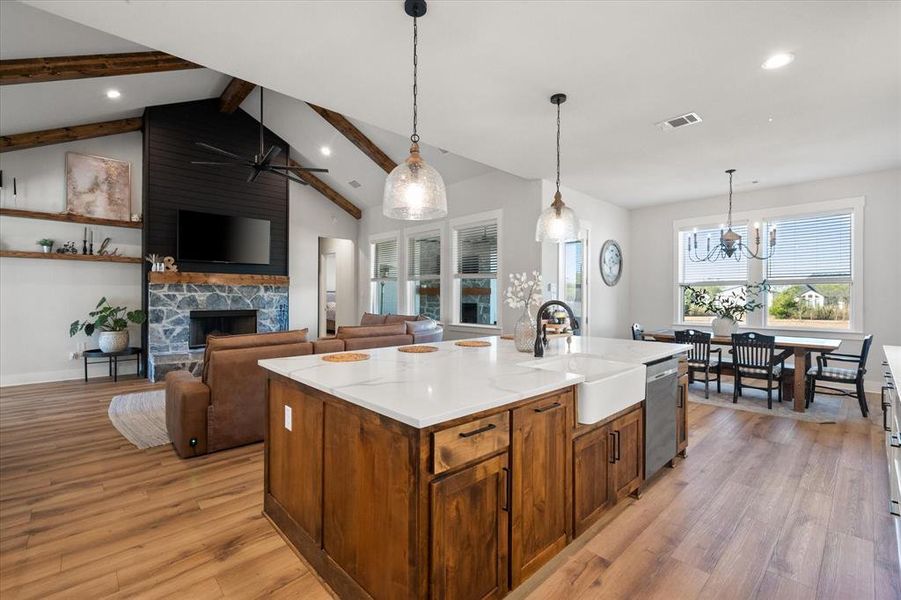 Kitchen featuring pendant lighting, brown cabinetry, light wood-style flooring, a stone fireplace, and recessed lighting