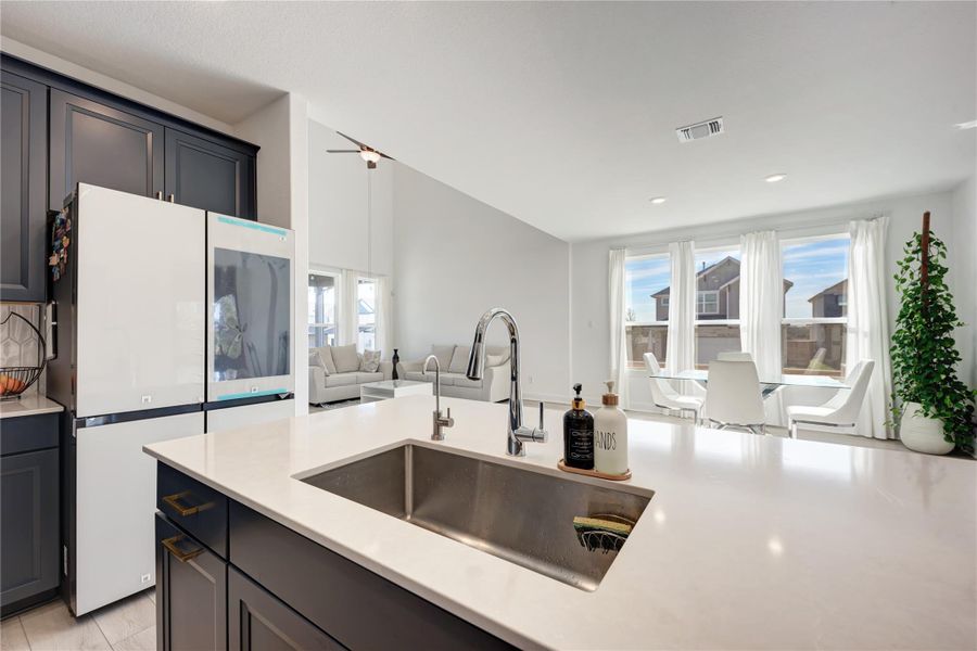 Open-concept interior featuring a large kitchen island with an undermount sink, dark cabinetry with brass hardware, vaulted ceilings in the living area, and multiple windows providing ample ambient light