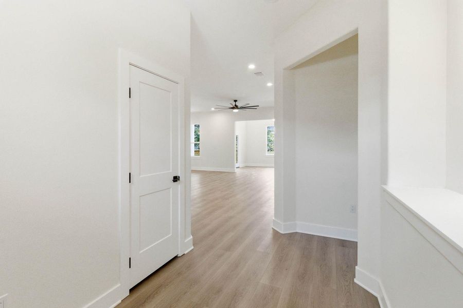 A clean, modern hallway leads to an open living area with recessed lighting and a ceiling fan. A clean, modern hallway leads to an open living area with recessed lighting and a ceiling fan.