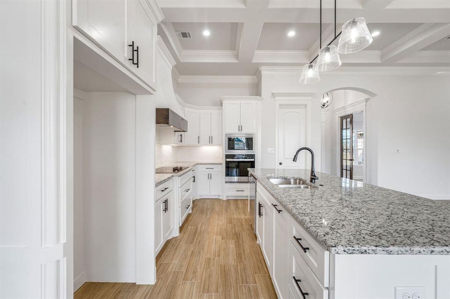 Kitchen with white cabinets, an island with sink, sink, hanging light fixtures, and oven