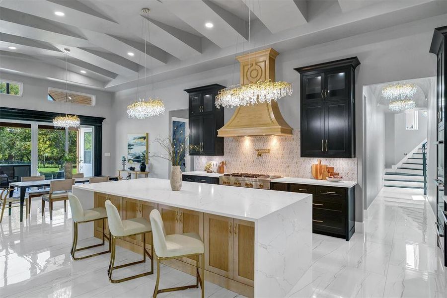 Kitchen with backsplash, a kitchen island, light stone counters, and a notable chandelier