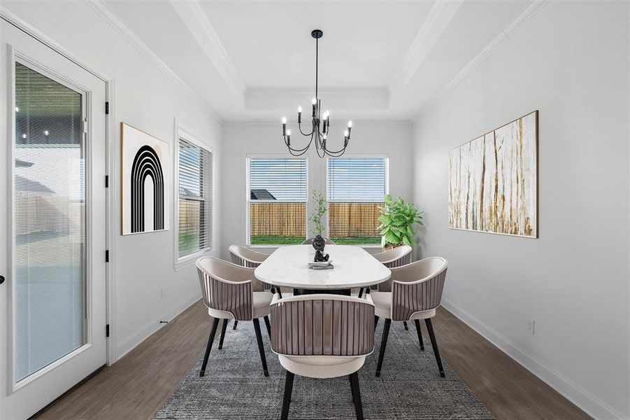 Dining space with dark wood finished floors, ornamental molding, a raised ceiling, and a chandelier. Virtually staged Dining space with dark wood finished floors, ornamental molding, a raised ceiling, and a chandelier. Virtually staged