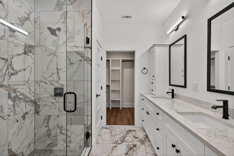 Full bath with light marble finish flooring, double vanity, a spacious closet, and a marble finish shower Full bath with light marble finish flooring, double vanity, a spacious closet, and a marble finish shower