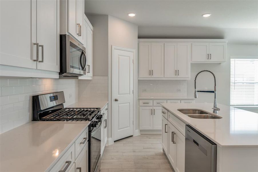 Modern kitchen featuring white shaker cabinetry, stainless steel appliances, light countertops, subway tile backsplash, and recessed lighting
