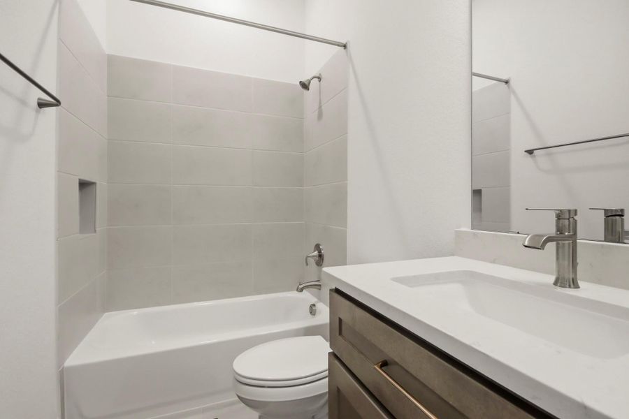 Sleek bathroom featuring a modern vanity with a polished countertop and a spacious tub surrounded by contemporary tilework.
