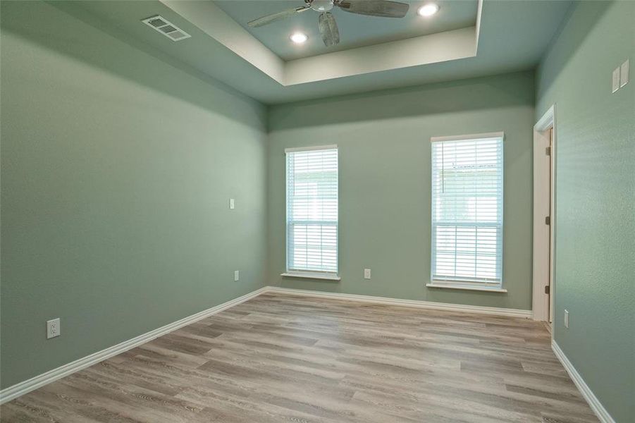 Unfurnished room featuring plenty of natural light, ceiling fan, light hardwood / wood-style flooring, and a tray ceiling