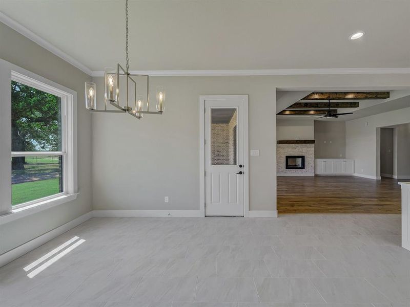 Spare room featuring a chandelier, crown molding, and a stone fireplace Spare room featuring a chandelier, crown molding, and a stone fireplace