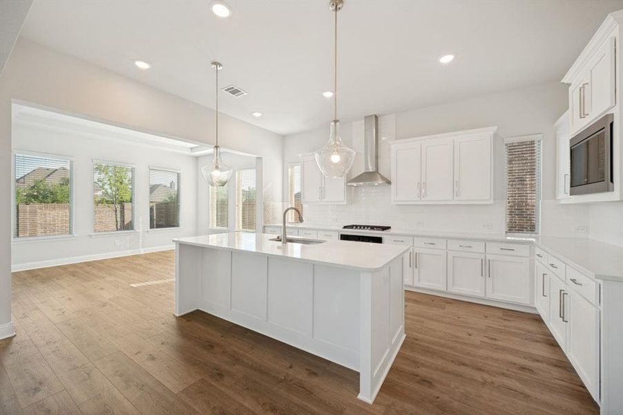 Modern kitchen featuring a large island with sink, white shaker cabinetry, stainless steel appliances, and wood-finish flooring
