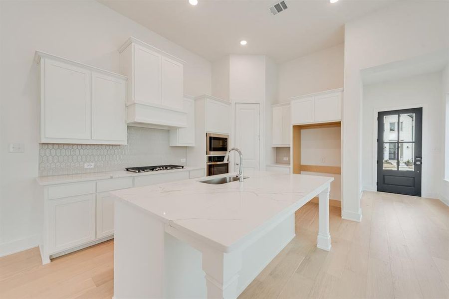 Kitchen featuring light stone counters, backsplash, white cabinetry, a kitchen breakfast bar, and an island with sink Kitchen featuring light stone counters, backsplash, white cabinetry, a kitchen breakfast bar, and an island with sink