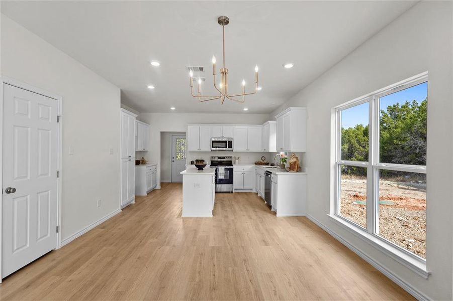 Kitchen with light countertops, a center island, white cabinets, hanging light fixtures, and a chandelier Kitchen with light countertops, a center island, white cabinets, hanging light fixtures, and a chandelier