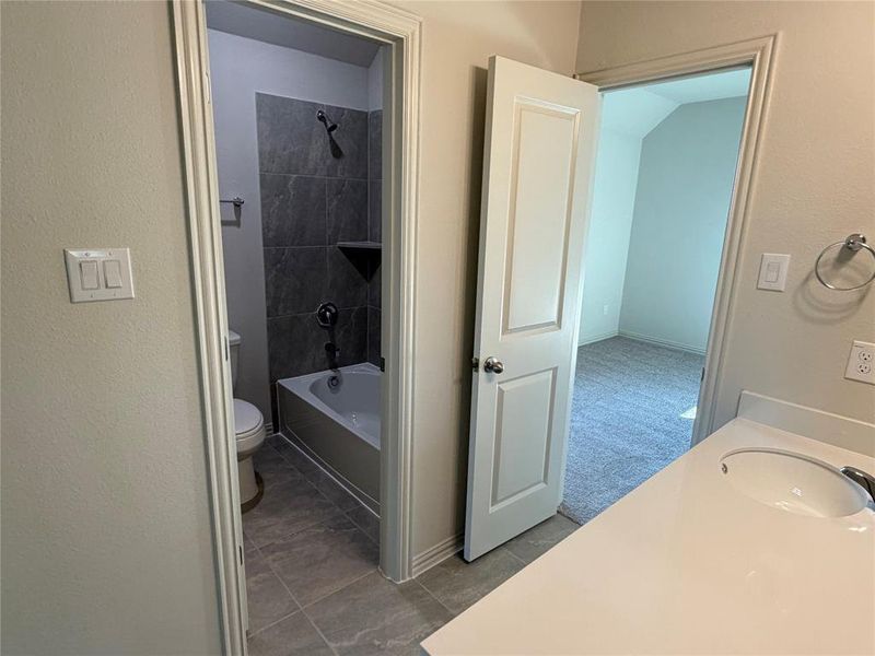 Bathroom vanity with a white countertop and integrated sink, featuring an adjacent full bathroom with a tiled shower/tub combination and a separate room with grey carpeting Bathroom vanity with a white countertop and integrated sink, featuring an adjacent full bathroom with a tiled shower/tub combination and a separate room with grey carpeting