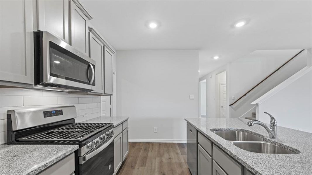 Kitchen featuring stainless steel appliances, light stone countertops, recessed lighting, gray cabinetry, and dark wood-style flooring Kitchen featuring stainless steel appliances, light stone countertops, recessed lighting, gray cabinetry, and dark wood-style flooring