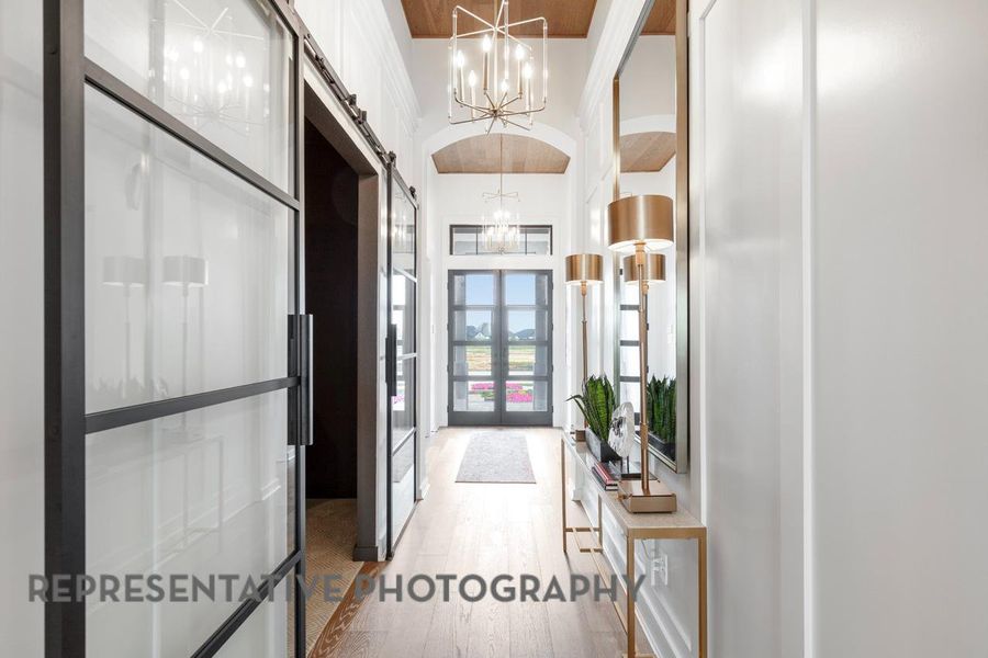Hallway with a high ceiling, a barn door, a chandelier, french doors, and light wood-type flooring