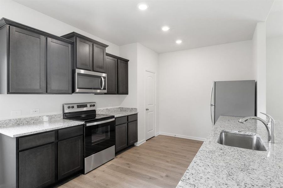 Kitchen featuring light wood-type flooring, appliances with stainless steel finishes, sink, and light stone counters