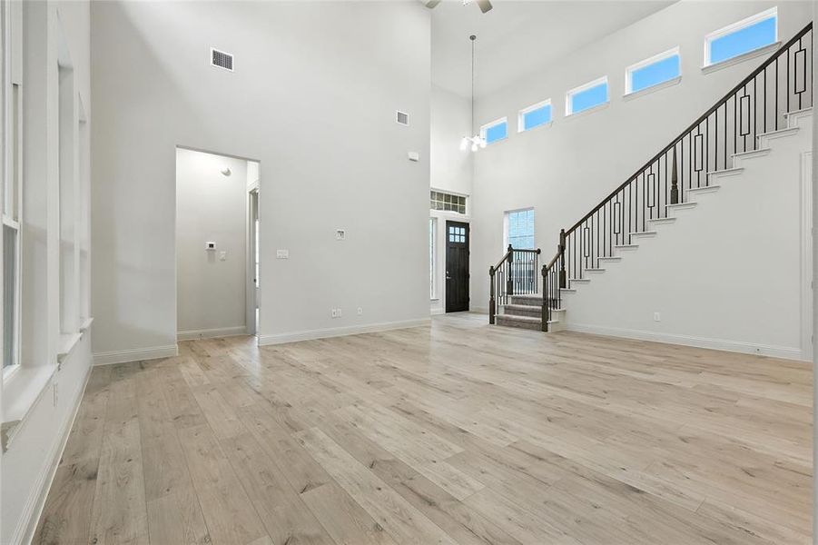 Unfurnished living room featuring stairs, light wood-style floors, and a high ceiling