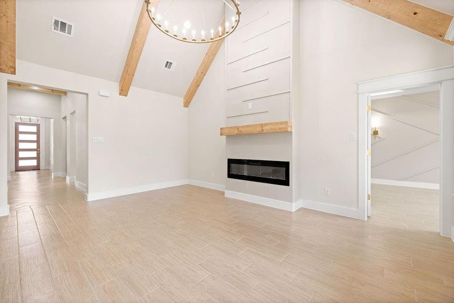 Unfurnished living room featuring visible vents, a glass covered fireplace, an inviting chandelier, light wood-style floors, and beam ceiling