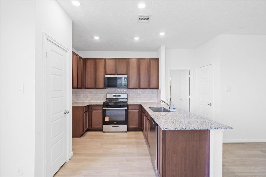 This spacious kitchen boasts high ceilings, White Woodmont Belmont cabinets, Granite Delicatus White countertops, stainless steel Whirlpool appliances, recessed lighting, windows with blinds, an added breakfast bar to kitchen countertop, and a pantry—all overlooking the expansive Great Room.