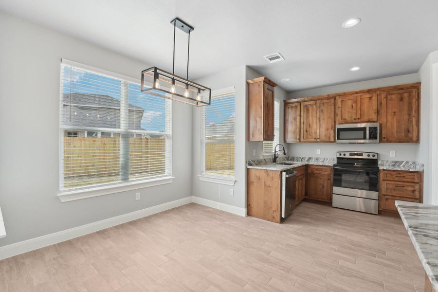 Kitchen featuring visible vents, light wood-style flooring, a sink, appliances with stainless steel finishes, and brown cabinets