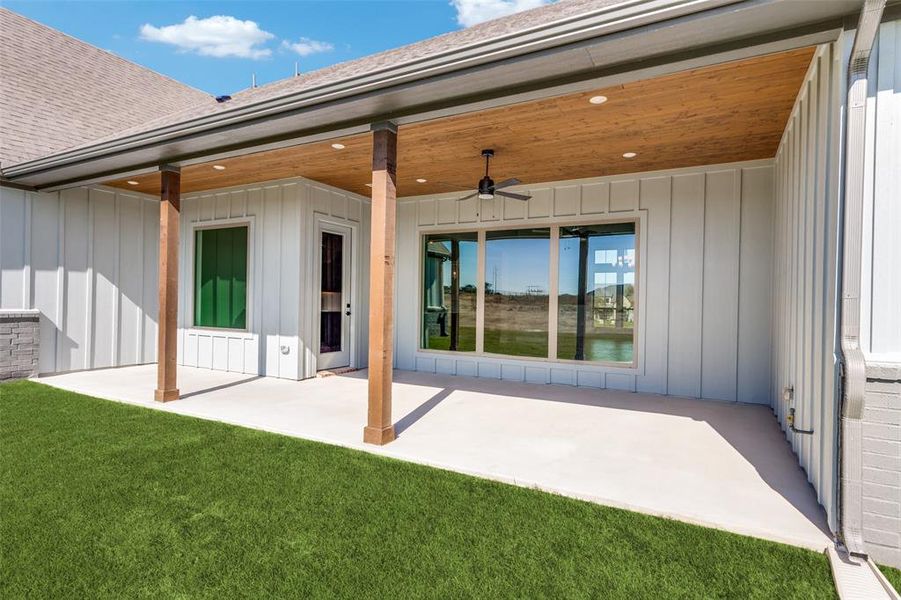 Back of property featuring board and batten siding, a ceiling fan, a patio area, roof with shingles, and a yard Back of property featuring board and batten siding, a ceiling fan, a patio area, roof with shingles, and a yard
