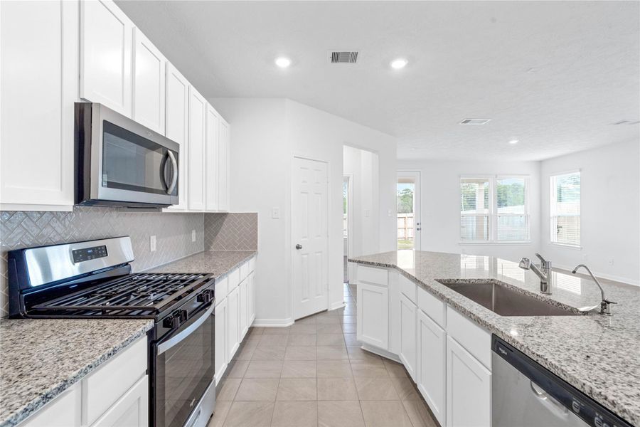 This bright, open kitchen is a chef's delight, complete with a large island, granite countertops, white Woodmont Dakota cabinets, Whirlpool stainless steel appliances, and modern Daltile backsplash.
