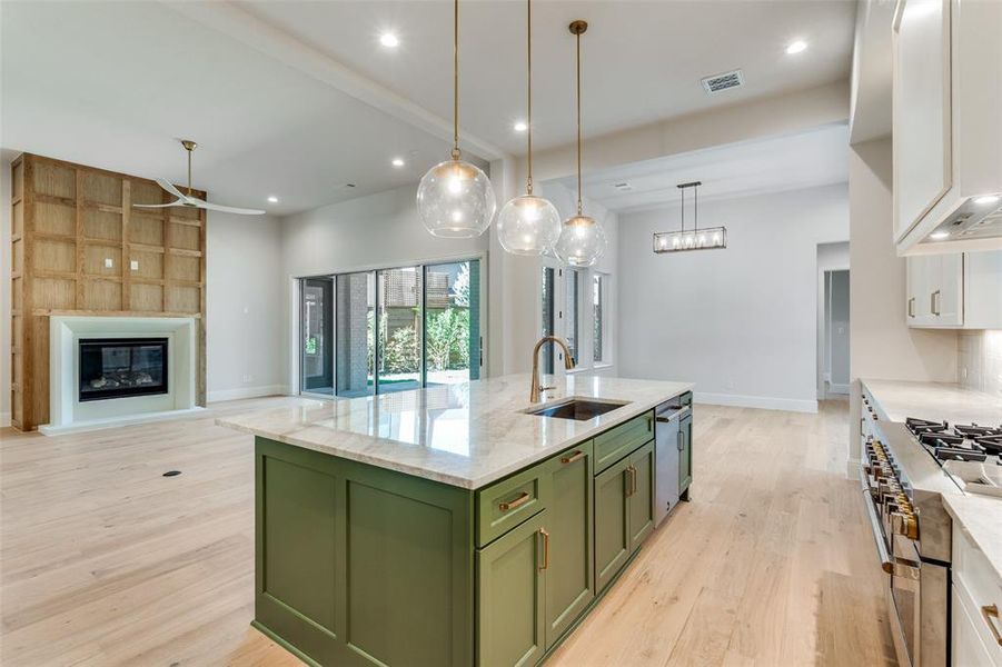 Kitchen featuring green cabinetry, light wood-style flooring, an island with sink, open floor plan, and light stone countertops Kitchen featuring green cabinetry, light wood-style flooring, an island with sink, open floor plan, and light stone countertops
