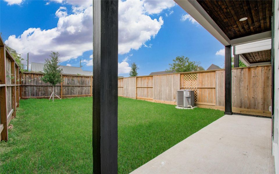 This photo showcases a backyard with a covered patio area, a neatly maintained lawn, and a wooden privacy fence, providing a cozy and private outdoor space.
