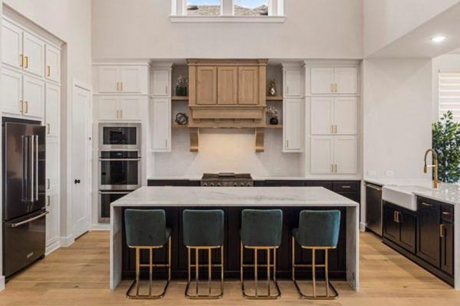 Kitchen with a high ceiling, light stone countertops, light wood-style floors, stainless steel appliances, and a kitchen breakfast bar