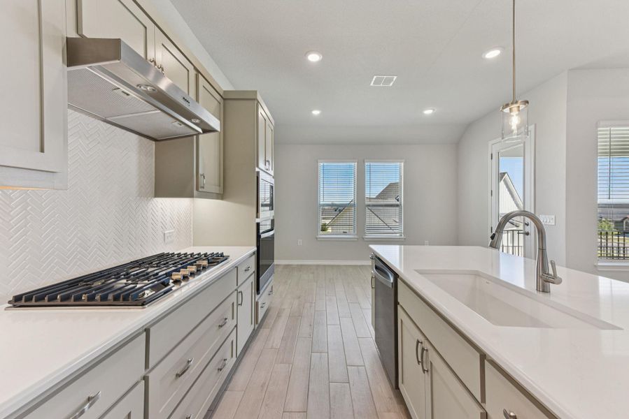 Kitchen with decorative light fixtures, under cabinet range hood, light wood finished floors, light stone countertops, and recessed lighting Kitchen with decorative light fixtures, under cabinet range hood, light wood finished floors, light stone countertops, and recessed lighting