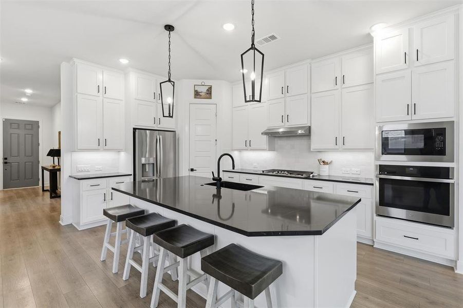 Kitchen featuring a large island with dark countertop, white shaker cabinetry, stainless steel appliances, and wood-finish flooring Kitchen featuring a large island with dark countertop, white shaker cabinetry, stainless steel appliances, and wood-finish flooring