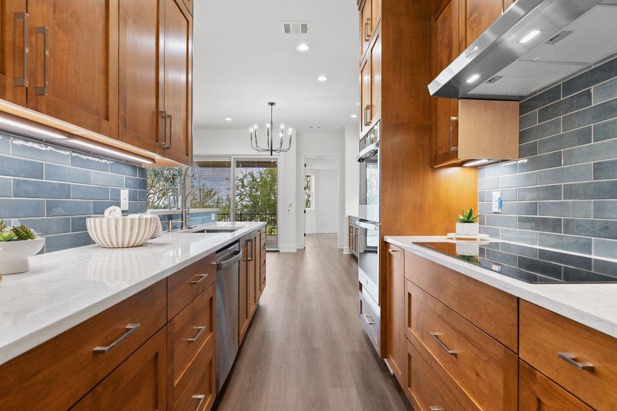 Kitchen featuring ventilation hood, a sink, brown cabinetry, wood finished floors, and decorative backsplash Kitchen featuring ventilation hood, a sink, brown cabinetry, wood finished floors, and decorative backsplash