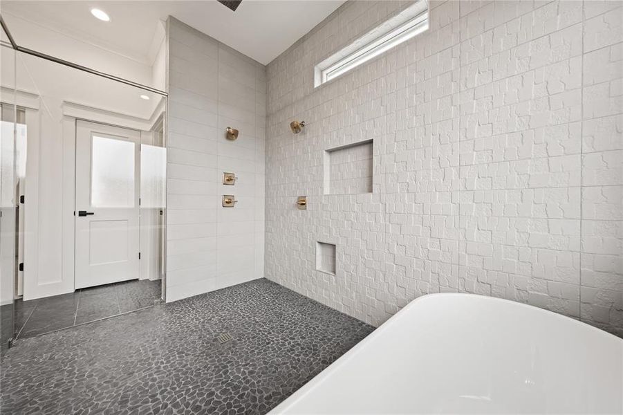 Spacious shower area featuring pebble-finish flooring, textured wall tiling, and brass fixtures