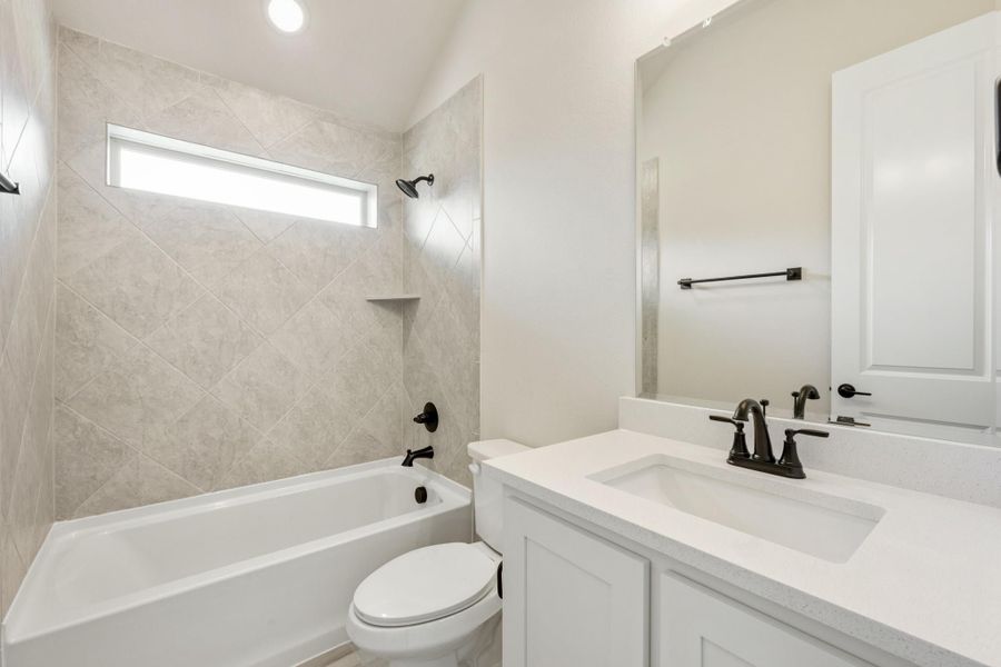 Bathroom with tiled tub-shower combo, white vanity with dark fixtures, and large mirror