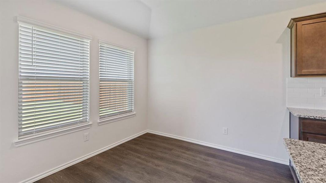 Dining area featuring two windows with blinds, wood-finish flooring, white baseboards, and a vaulted ceiling
