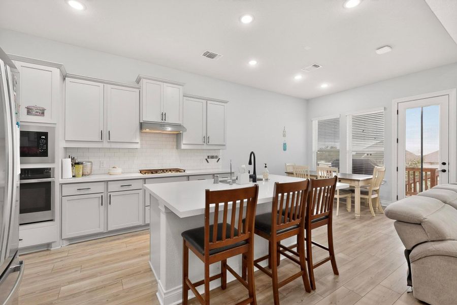 Kitchen with an island with sink, a kitchen breakfast bar, light wood-style flooring, tasteful backsplash, and recessed lighting