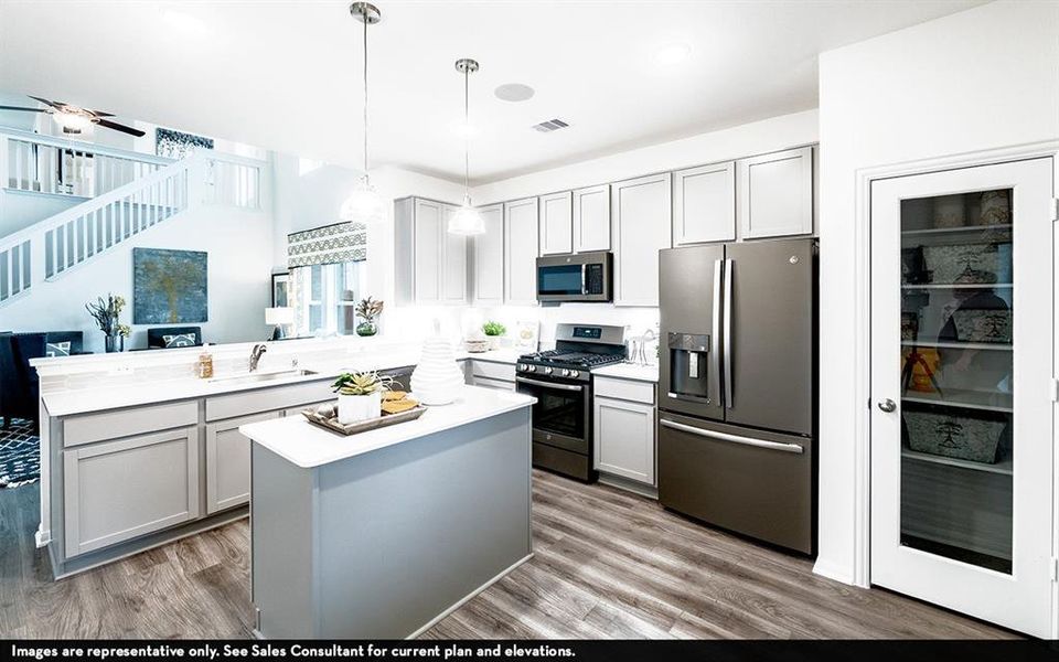 Kitchen featuring wood-finish flooring, light-toned cabinetry, a central island with countertop space, stainless steel appliances, and a pantry with a frosted glass door Kitchen featuring wood-finish flooring, light-toned cabinetry, a central island with countertop space, stainless steel appliances, and a pantry with a frosted glass door