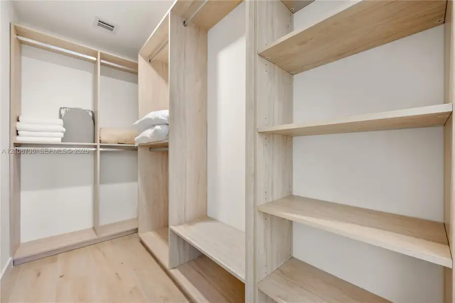 Walk-in closet featuring custom wood-finish shelving, integrated hanging rods, and wood-finish flooring Walk-in closet featuring custom wood-finish shelving, integrated hanging rods, and wood-finish flooring