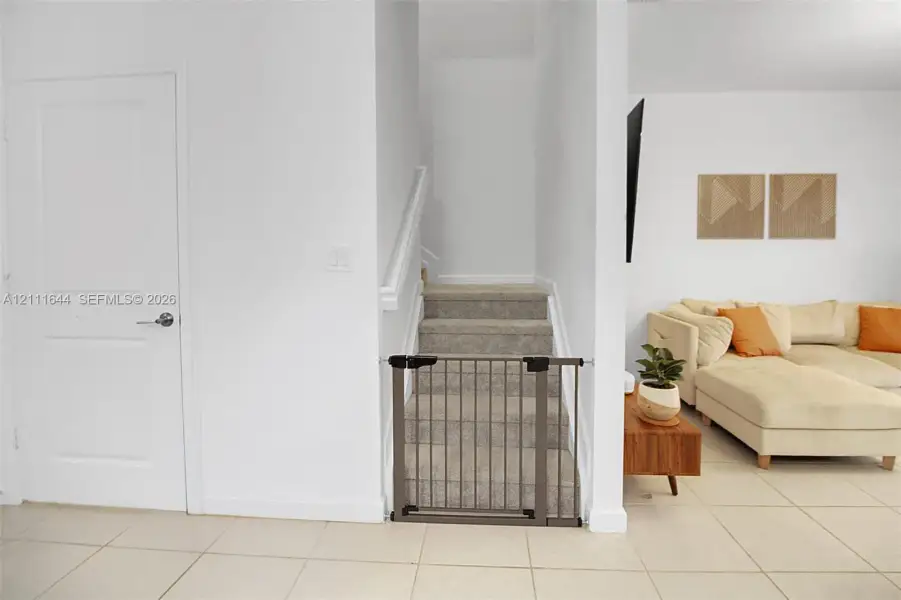 Neutral-toned ceramic tile flooring, staircase with carpeted treads, and painted white interior doors with satin nickel hardware Neutral-toned ceramic tile flooring, staircase with carpeted treads, and painted white interior doors with satin nickel hardware