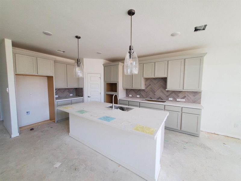 Kitchen featuring a sink, concrete flooring, an island with sink, and gray cabinetry