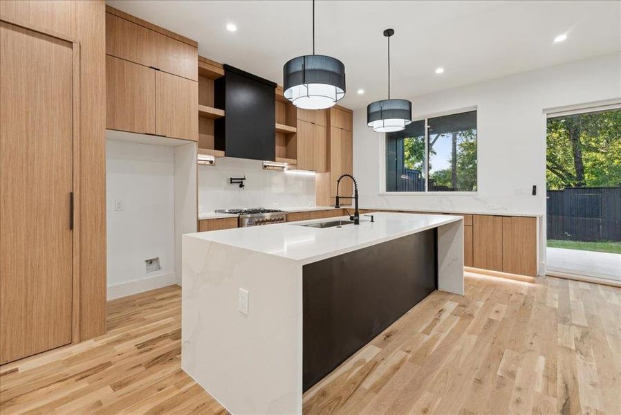 Kitchen with an island with sink, ventilation hood, sink, pendant lighting, and light hardwood / wood-style flooring