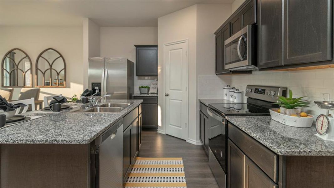 Kitchen featuring dark wood-finish cabinetry, stainless steel appliances, speckled stone countertops, and a subway tile backsplash