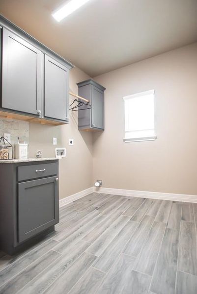 Laundry area with electric dryer hookup, washer hookup, cabinet space, and light wood-style flooring Laundry area with electric dryer hookup, washer hookup, cabinet space, and light wood-style flooring