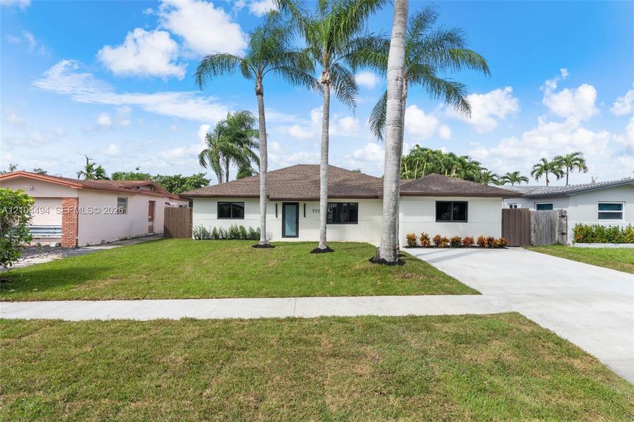 Single-story exterior featuring a shingled roof, stucco finish, concrete driveway, and mature palm trees