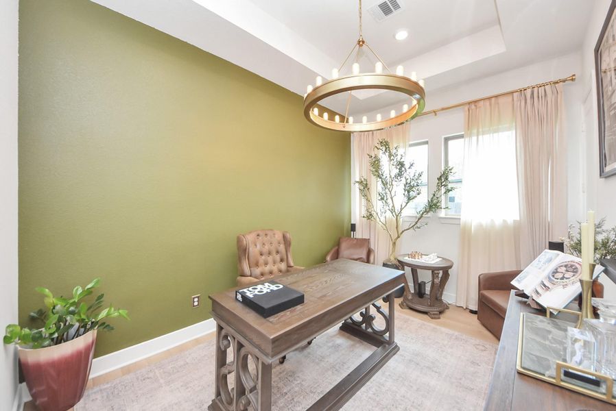 Elegant home office featuring a rich green accent wall, sophisticated leather chair, and a stylish chandelier. Natural light pours in through the window, highlighting the room's tasteful decor and inviting atmosphere.