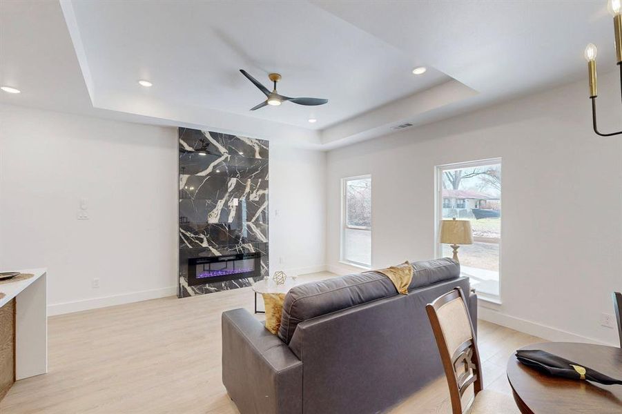 Living room featuring a tray ceiling, ceiling fan, light wood-type flooring, and a premium fireplace