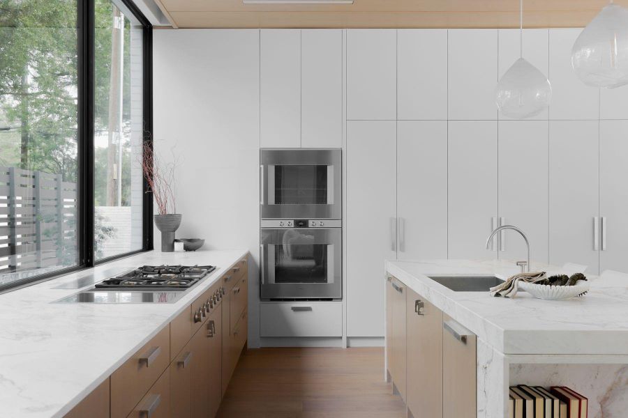Kitchen with modern cabinets, light stone counters, an island with sink, hanging light fixtures, and dark wood-type flooring