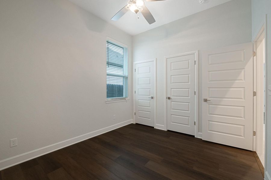 Unfurnished bedroom with multiple closets, dark wood-style flooring, and ceiling fan