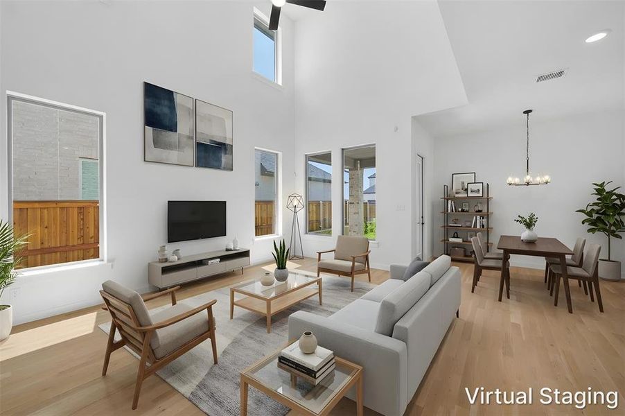 Spacious open-concept living area featuring a double-height ceiling, wood-finish flooring, abundant natural light from multiple windows, and a dedicated dining space. Virtually staged