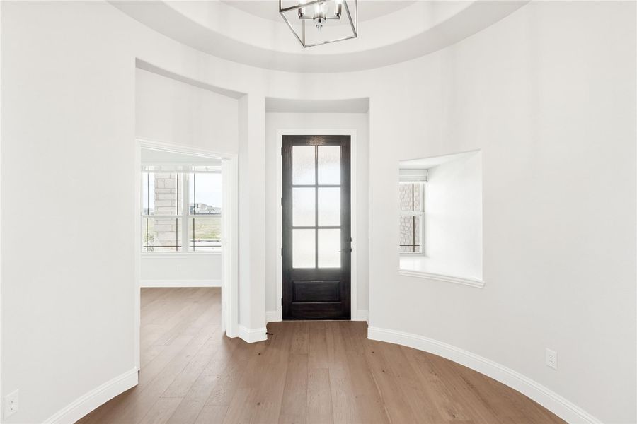 Rounded entryway with dark wood front door, hardwood floors, tray ceiling, and modern pendant light fixture