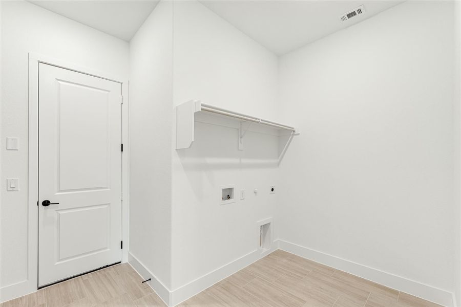 Laundry room with white walls, built-in shelf with rod, washer and dryer hookups, and light wood-look tile floor. Laundry room with white walls, built-in shelf with rod, washer and dryer hookups, and light wood-look tile floor.